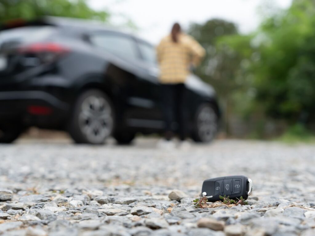 Car key fob on gravel with stranded driver blurred in the background