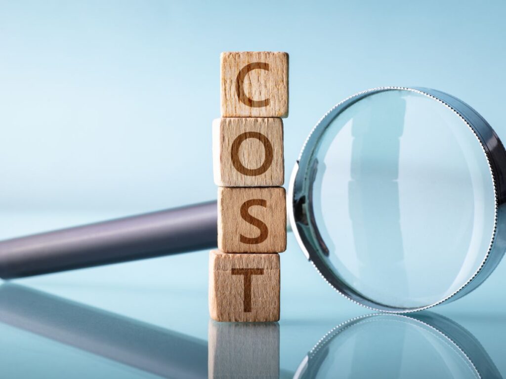 Wooden blocks spelling COST beside a magnifying glass