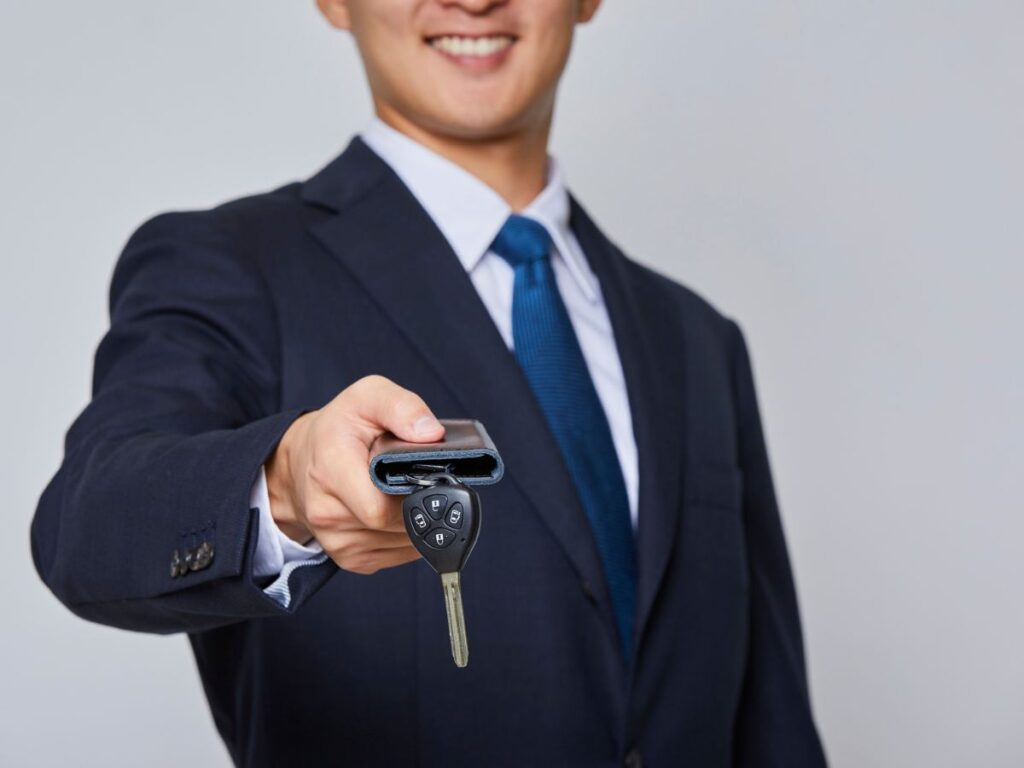 Person in suit handing over a car key fob and wallet toward the viewer