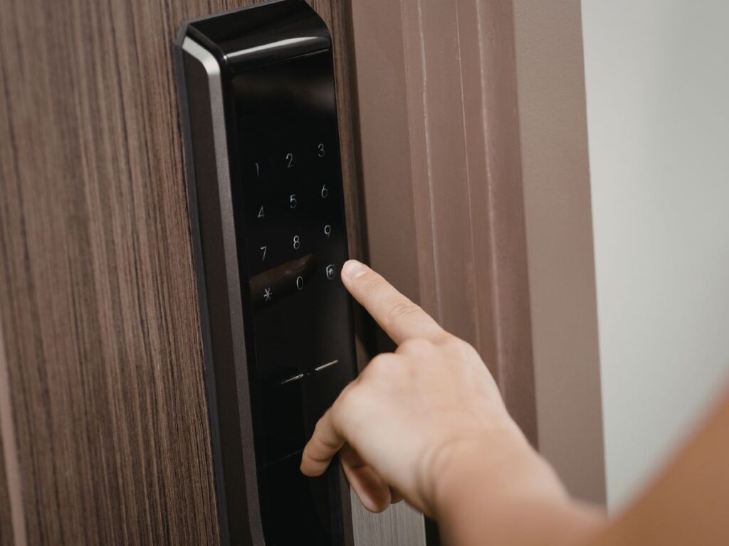 Hand entering a code on a black smart lock mounted on a wood door