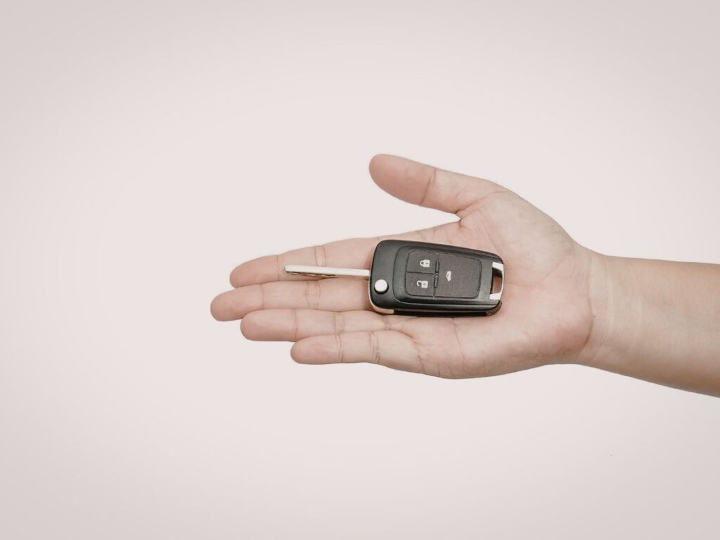 Open hand holding a car key fob on a plain background