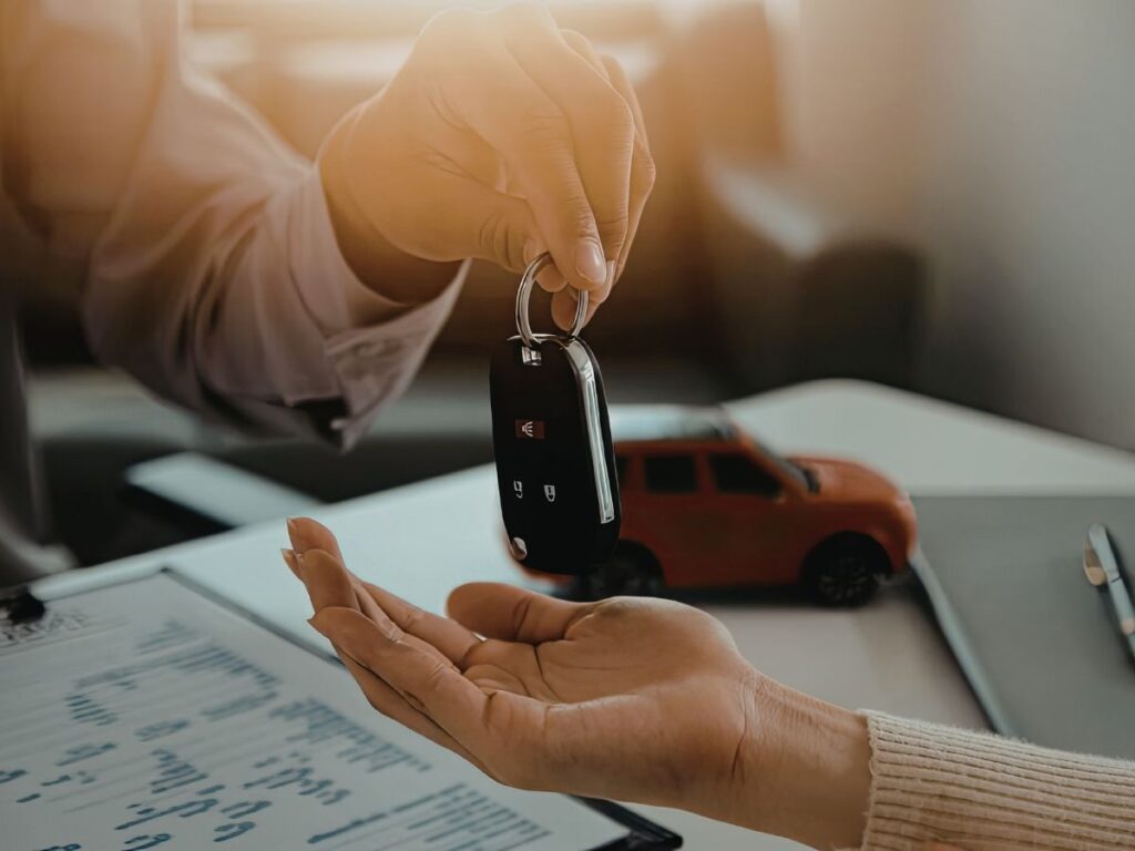 Handing over a car key fob above paperwork and a model car