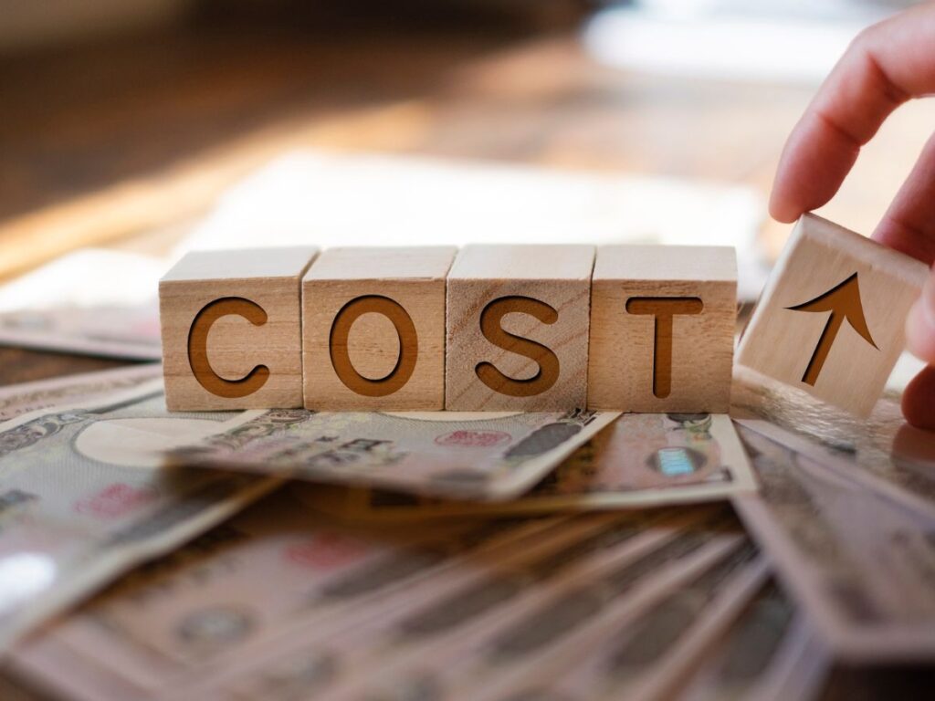 Wooden blocks spelling “COST” placed on top of scattered cash