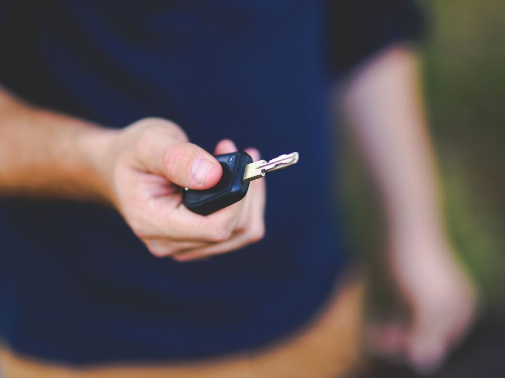 Hand holding out a car key against a blurred background